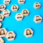 Sechseckige Holzplättchen mit Mitarbeitersymbolen auf blauem Hintergrund veranschaulichen Personalplanung Betriebsrat sowie die Organisation und Verteilung von Personalressourcen.